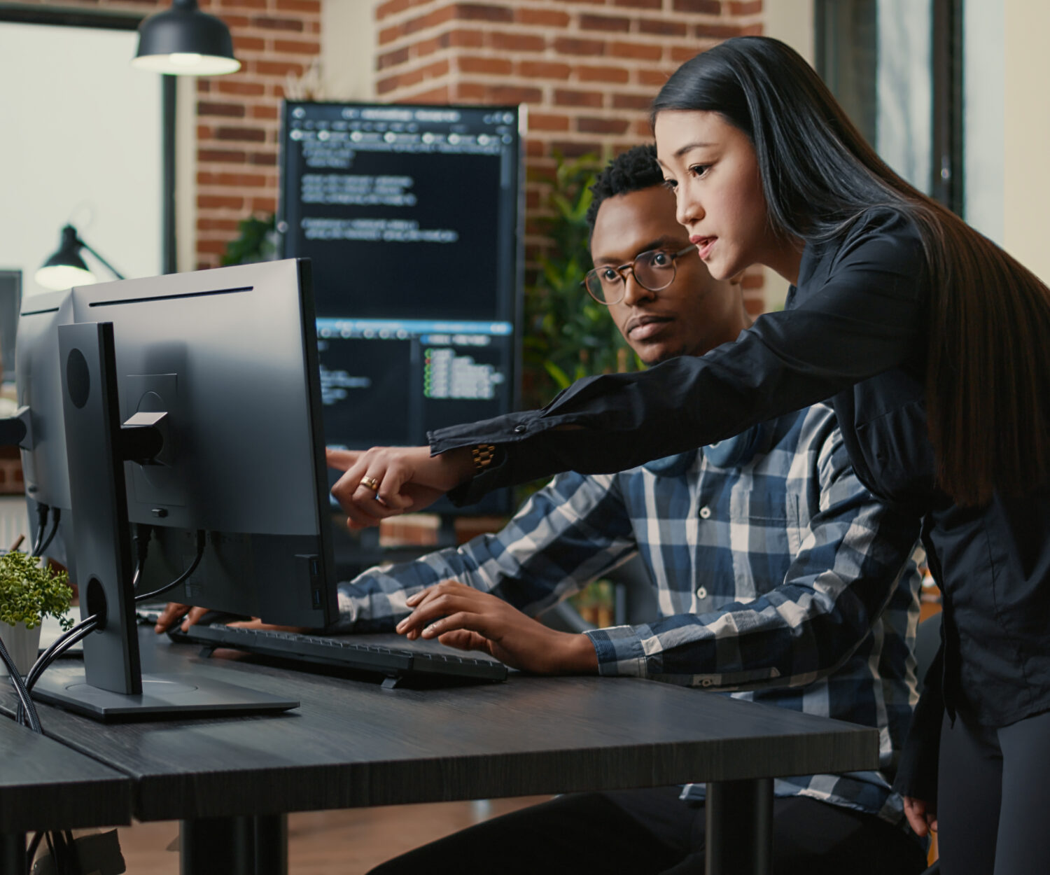 Two programers holding laptop with coding interface walking towards desk and sitting down talking about online cloud computing. Software developers team discussing algorithms on computer screen.