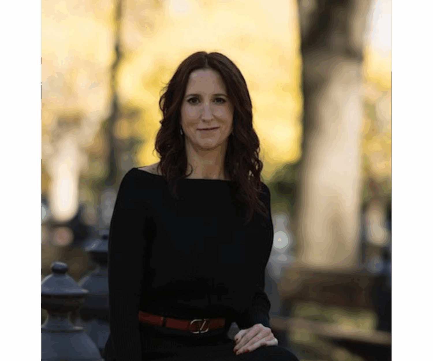 Tracy Ongena seated outdoors in a black dress with autumn trees in the background